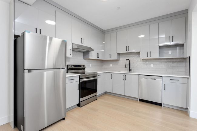 Kitchen with light wood finished floors, under cabinet range hood, light countertops, appliances with stainless steel finishes, and a sink | Image 31