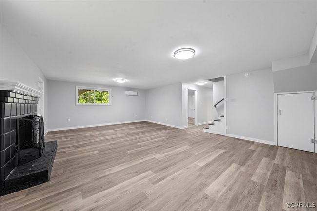 Unfurnished living room featuring stairs, light wood-style flooring, a fireplace with raised hearth, baseboards, and a wall unit AC | Image 26