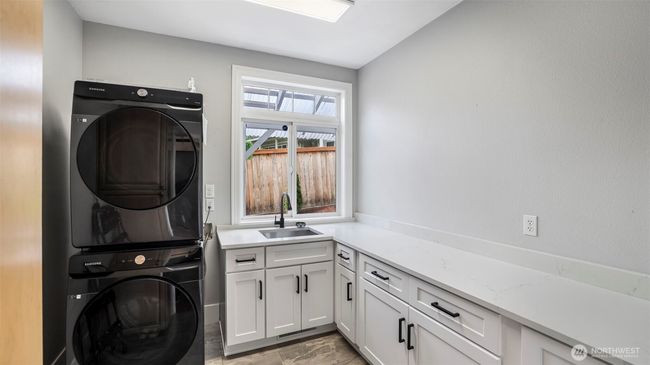 A generously sized laundry area featuring crisp white cabinetry with black handles, ample storage, and a built-in sink for added functionality | Image 23