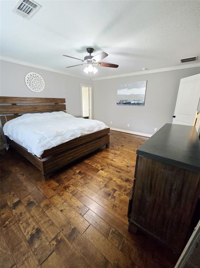 This primary bedroom features hardwood floors, neutral gray walls, and a ceiling fan, creating a cozy and inviting atmosphere. | Image 25