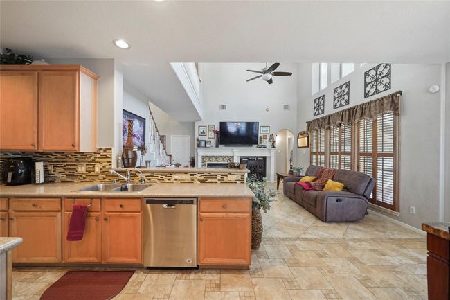 This inviting open-concept living space features a modern kitchen with stainless steel appliances and a tile backsplash. Adjacent is a cozy living room with high ceilings, a ceiling fan, and large windows offering plenty of natural light. The room includes a fireplace perfect for relaxation and entertaining. | Image 14