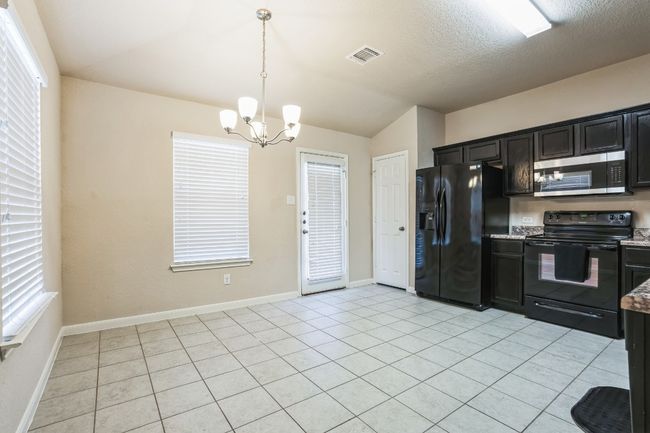 Kitchen with lofted ceiling, a textured ceiling, light tile patterned floors, hanging light fixtures, and black appliances | Image 8