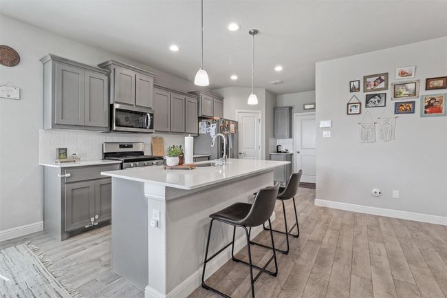 Kitchen with appliances with stainless steel finishes, gray cabinets, light wood-type flooring, a breakfast bar, and recessed lighting | Image 5