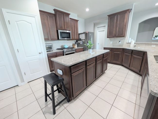 Kitchen featuring stainless steel appliances, light tile patterned flooring, backsplash, dark brown cabinetry, and recessed lighting | Image 25
