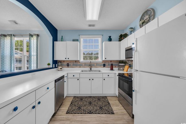 Kitchen with a sink, a textured ceiling, decorative backsplash, appliances with stainless steel finishes, and visible vents | Image 8