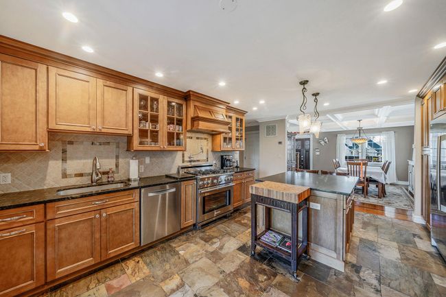 Kitchen featuring stainless steel appliances, decorative backsplash, a sink, stone tile flooring, and brown cabinetry | Image 6
