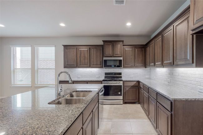 Kitchen with stainless steel appliances, a sink, light stone counters, backsplash, and recessed lighting | Image 8