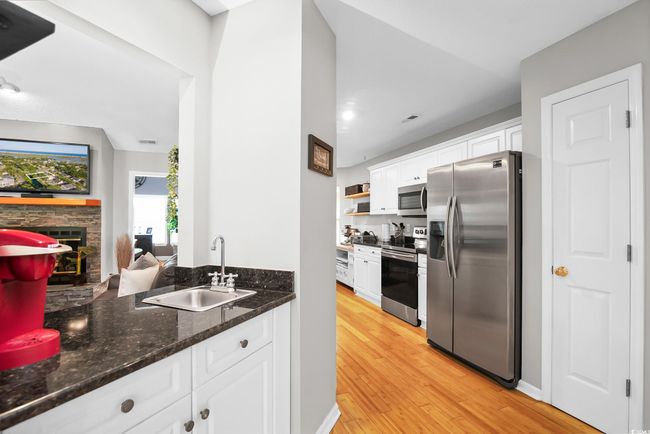 Kitchen featuring stainless steel appliances, white cabinets, a fireplace, light wood-style flooring, and recessed lighting | Image 13