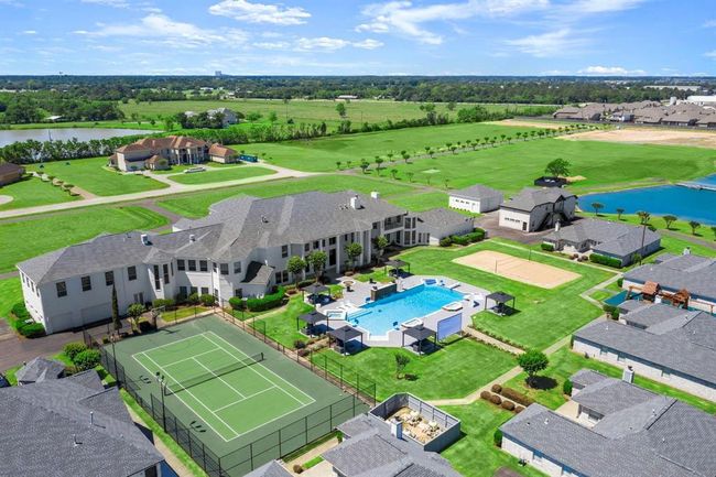 This aerial photo showcases a luxurious residential property with a spacious backyard that includes a swimming pool, a tennis court, and a volleyball court, all surrounded by well-manicured lawns and situated in a community with a picturesque lake view. | Image 38