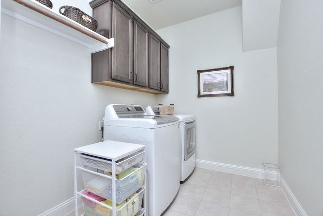 Clothes washing area with washer and clothes dryer, light tile patterned floors, cabinet space, and baseboards | Image 29