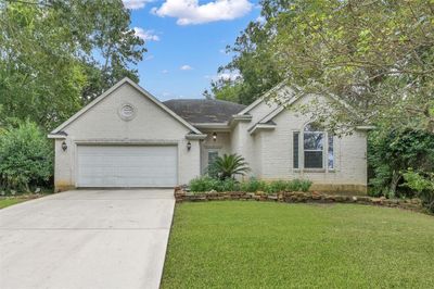 Enchanting single-story residence with a spacious two-car garage, boasting a radiant brick exterior, expansive windows, and a pristine lawn set against a backdrop of towering trees. | Image 3