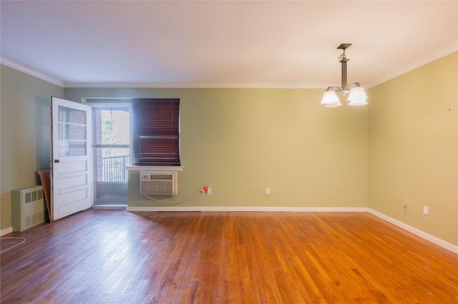 Empty room with baseboards, an inviting chandelier, an AC wall unit, radiator, and wood finished floors | Image 13