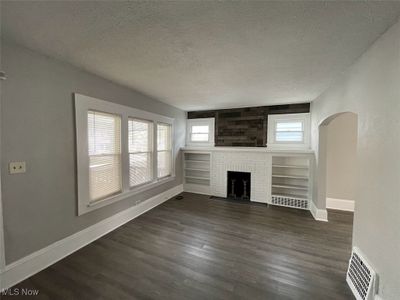 Unfurnished living room with a textured ceiling, dark hardwood / wood-style flooring, and a brick fireplace | Image 2