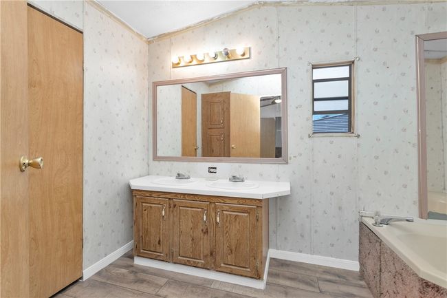 Full bathroom with wood finished floors, double vanity, a garden tub, crown molding, and wallpapered walls | Image 15
