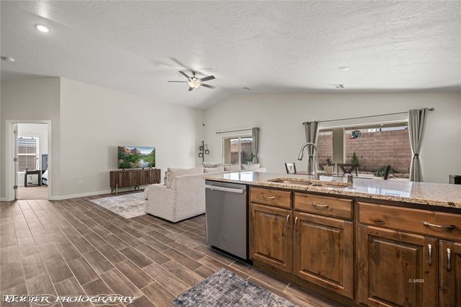 Kitchen featuring stainless steel dishwasher, a sink, vaulted ceiling, a ceiling fan, and light stone countertops | Image 32