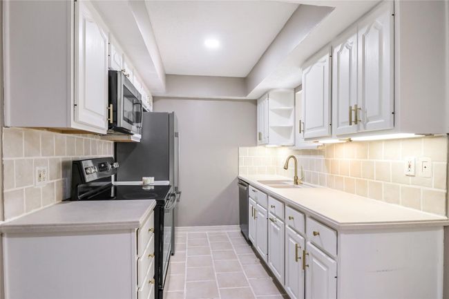 Kitchen with stainless steel appliances, white cabinets, a sink, light countertops, and decorative backsplash | Image 13