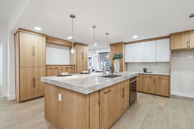 Kitchen featuring light wood-type flooring, an island with sink, a sink, tasteful backsplash, and stainless steel dishwasher | Image 15