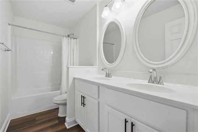 Crisp and clean full bathroom featuring a double vanity with white cabinetry, and modern chrome fixtures. Includes a combination tub and shower with a sleek white surround and rich wood-look LVP flooring for a warm touch. Mirrors not included. | Image 28