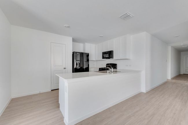 Kitchen with black appliances, light wood-style flooring, a peninsula, white cabinets, and light countertops | Image 10
