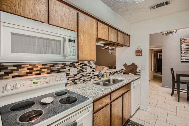 Kitchen with white appliances, tasteful backsplash, stone tile floors, a textured ceiling, and brown cabinets | Image 8