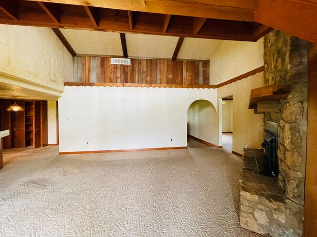 unfurnished living room featuring high vaulted ceiling, carpet flooring, a fireplace, wooden walls, and baseboards | Image 10