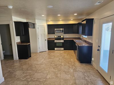 Kitchen featuring stainless steel appliances, dark stone countertops, a textured ceiling, and sink | Image 3