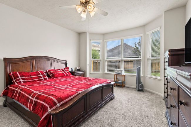 This bedroom features a cozy carpeted floor, a large window bay providing ample natural light, and a ceiling fan for comfort. It is furnished with a wooden bed frame and matching dresser, creating a warm and inviting atmosphere. | Image 15