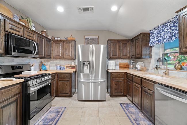 Kitchen featuring appliances with stainless steel finishes, vaulted ceiling, backsplash, dark brown cabinetry, and wood counters | Image 14