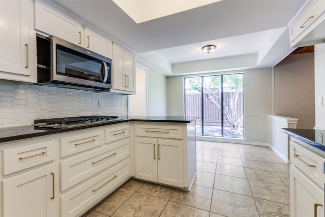 Kitchen with stainless steel appliances, tasteful backsplash, dark stone counters, and white cabinets | Image 15