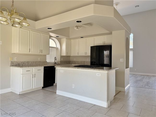 Kitchen featuring a chandelier, light stone counters, white cabinets, black appliances, and a sink | Image 9