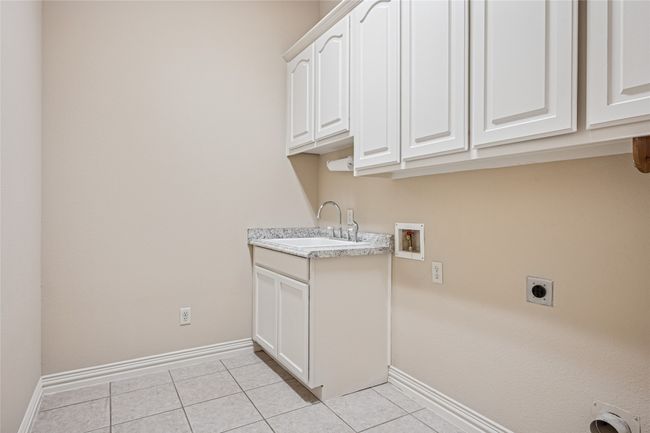Washroom with electric dryer hookup, washer hookup, built-in cabinet space, and light tile patterned flooring | Image 31