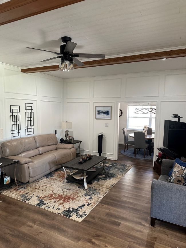 Living area with a decorative wall, ceiling fan, crown molding, and dark wood finished floors | Image 13