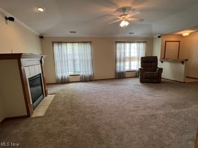 Living area featuring crown molding, ceiling fan, light carpet, and a tile fireplace | Image 9