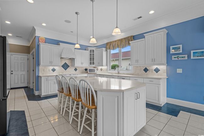 Kitchen with premium range hood, a kitchen bar, white microwave, white cabinetry, and ornamental molding | Image 11