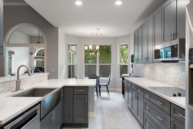 Kitchen with light stone counters, stainless steel appliances, a sink, tasteful backsplash, and a notable chandelier | Image 13