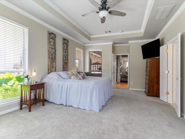 Bedroom featuring a tray ceiling, light carpet, multiple windows, and crown molding | Image 19