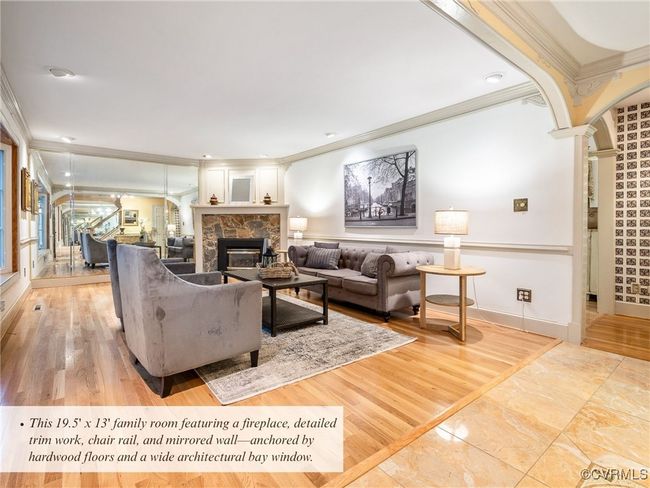 This 19.5' x 13' family room featuring a fireplace, detailed trim work, chair rail, and mirrored wall—anchored by hardwood floors and a wide architectural bay window. | Image 8