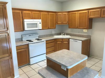 Kitchen with white appliances, a kitchen island, light tile patterned floors, and sink | Image 2