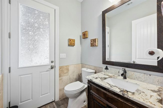 Half bathroom with vanity, toilet, tile wall wainscoting and quick access to the back patio and pool. | Image 31