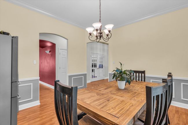 Dining room with a chandelier, arched walkways, crown molding, a wainscoted wall, and light wood-type flooring | Image 7