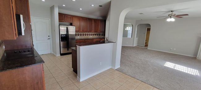 Kitchen with light tile patterned floors, light colored carpet, recessed lighting, stainless steel fridge with ice dispenser, and open floor plan | Image 7