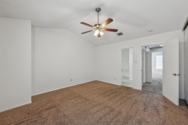 Unfurnished bedroom with vaulted ceiling, ensuite bathroom, carpet floors, visible vents, and ceiling fan | Image 15