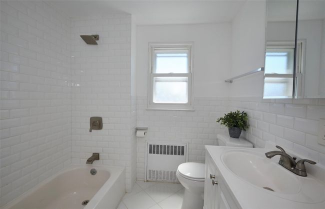 Bathroom featuring radiator heating unit, tile patterned flooring, vanity, toilet, and tile walls | Image 13