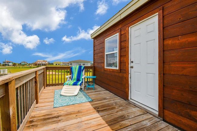 This photo showcases the back sun deck with a lounge chair and small table, perfect for relaxing. The area offers a clear view of a grassy landscape and neighboring houses, and bay views. | Image 22