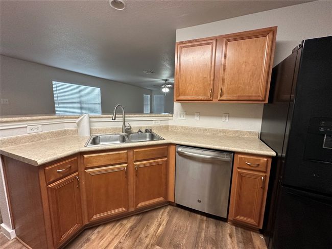 Kitchen with freestanding refrigerator, stainless steel dishwasher, wood finished floors, a peninsula, and light countertops | Image 11
