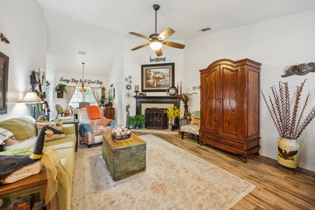 Living area featuring a ceiling fan, light wood finished floors, a fireplace with raised hearth, and high vaulted ceiling | Image 7