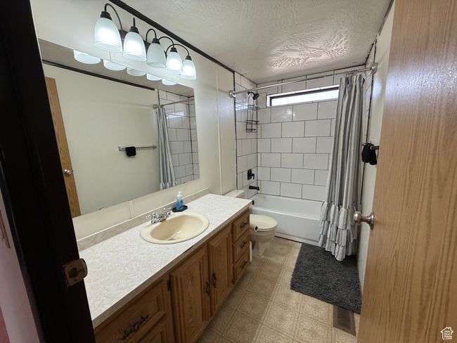 Full bath with a textured ceiling, vanity, toilet, shower / bath combo with shower curtain, and tile patterned floors | Image 11