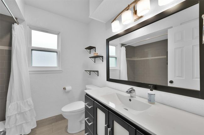 The remodeled Secondary Bathroom has a vanity with drawers and cabinet for storage, a framed mirror and updated light fixture. To the right just out of the picture is the modern tub/shower with decorative tile and product niche. There is also an additional built-in cabinet with laundry hamper tucked away behind the door. | Image 21