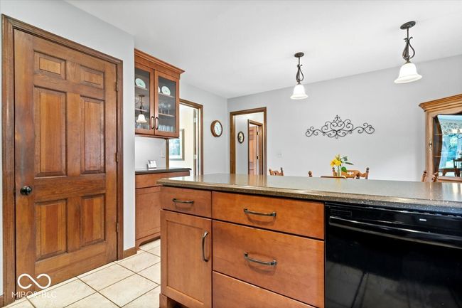 kitchen with brown cabinets, hanging light fixtures, glass insert cabinets, and light tile patterned flooring | Image 14
