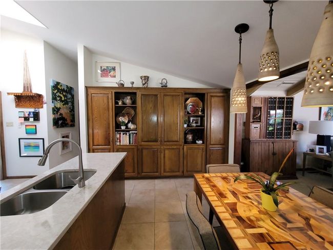 Kitchen with decorative light fixtures, lofted ceiling, open shelves, light tile patterned flooring, and a sink | Image 23